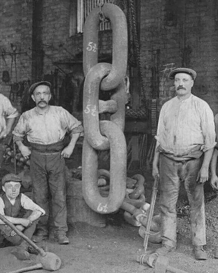 Black and white photo of men in a workshop with large metal chain links, learning weird things about history.