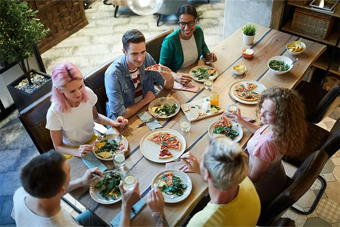Group of friends enjoying pizza and salad at a lively dinner, sharing laughs and conversation about relationship icks.