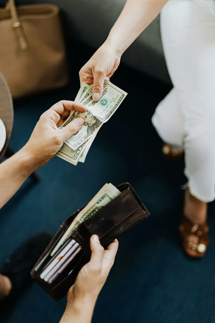 Hand passing cash to another person holding a wallet, illustrating disrespectful actions from partner’s family.