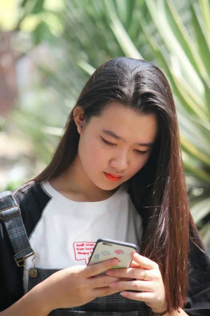 Young woman looking upset while reading a message on her phone about disrespect from partner’s family outdoors.