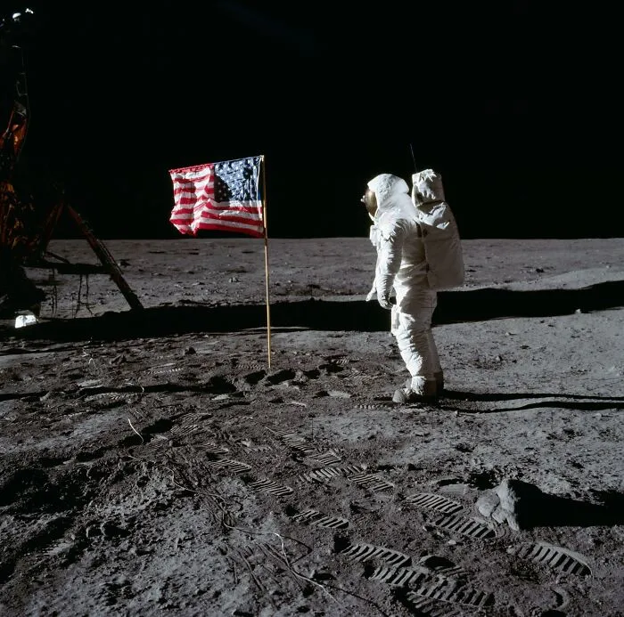 Astronaut standing on the moon next to the American flag during an Apollo mission with visible lunar footprints.
