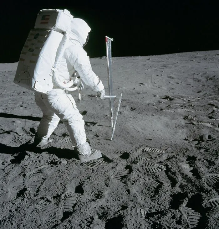 Apollo mission astronaut collecting lunar soil samples on the moon’s surface with footprints visible in the dust.