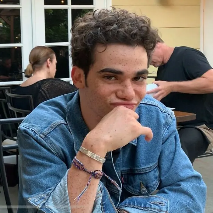 Young man with curly hair and freckles wearing a denim jacket, captured in one of the last known photos of famous people.