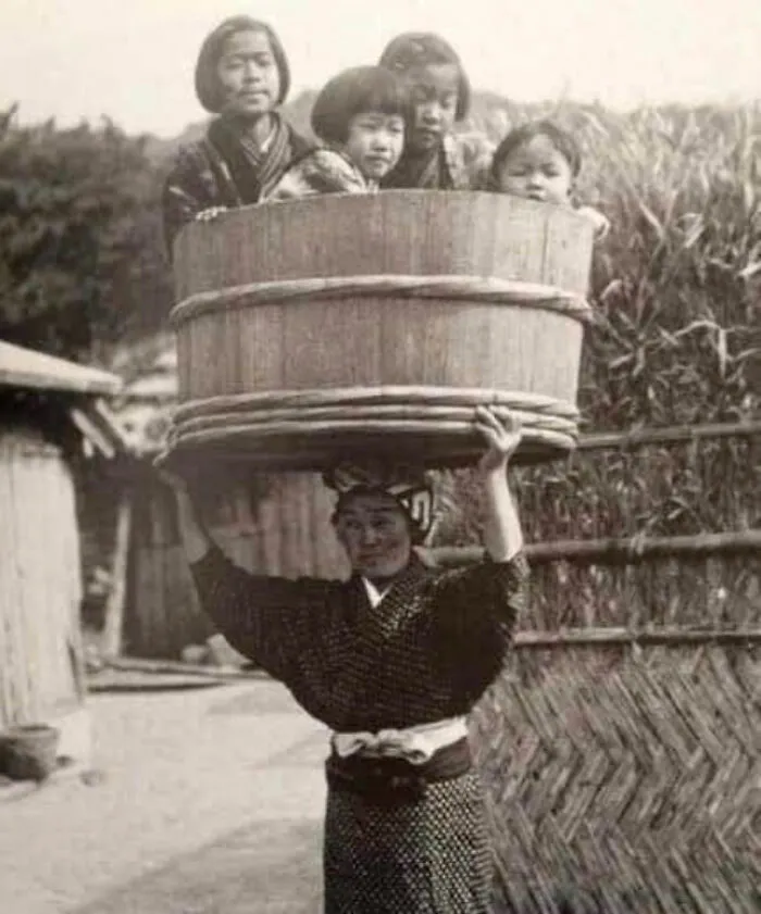 A Japanese Woman Carrying Her Children In A Bucket On Her Head, Japan, Ca. 1900s