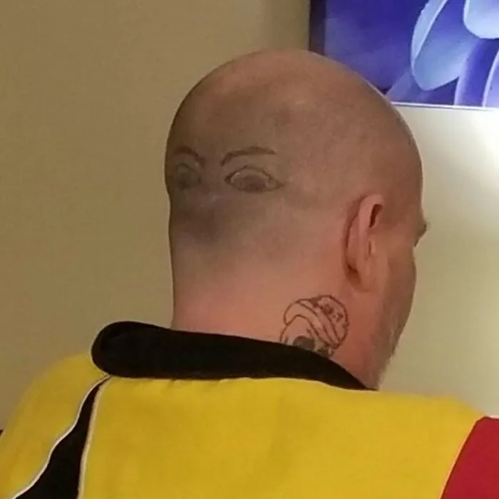 Man with bizarre tattoo of eyes on the back of his shaved head, showcasing strange choices people made while getting tattoos.