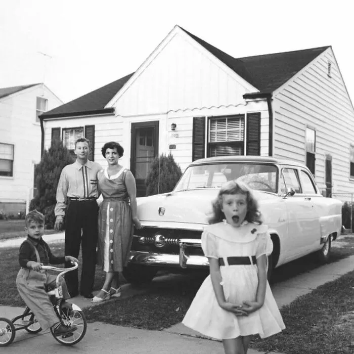 Vintage black and white photo showing a family and classic car in front of a suburban home, illustrating weird things about history.