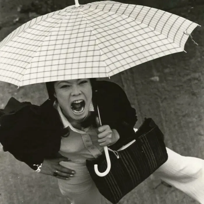 Black and white photo of a woman holding an umbrella screaming, featured in an Instagram account sharing weird things about history.