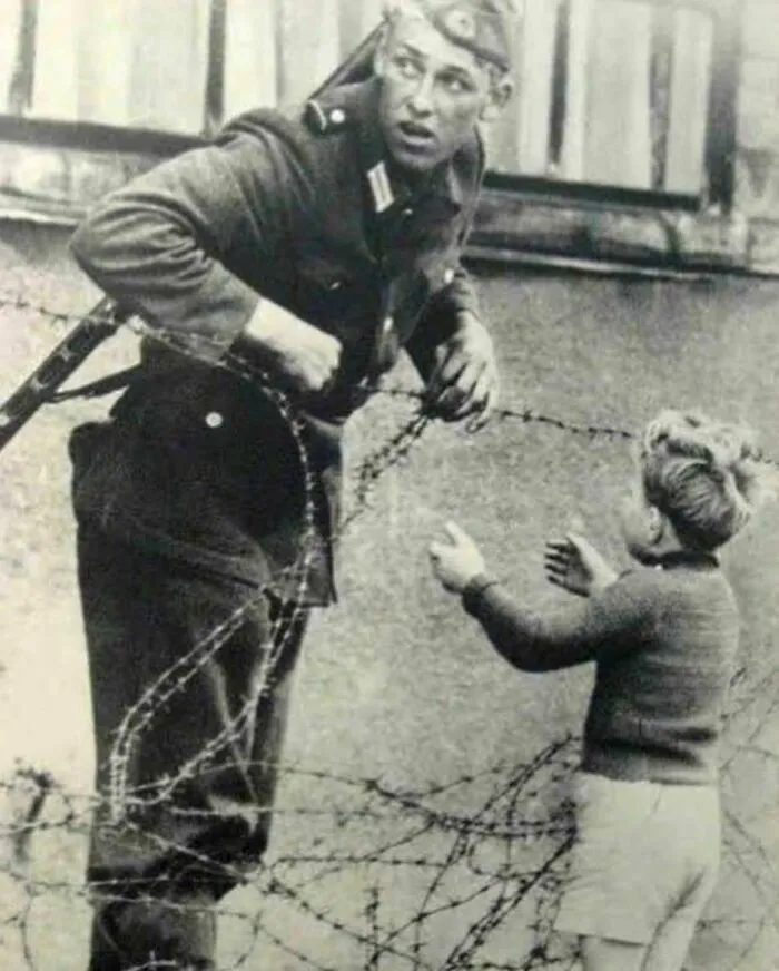 Un soldado de Alemania Oriental ayuda a un niño a cruzar el Muro de Berlín el día de su construcción en 1961.