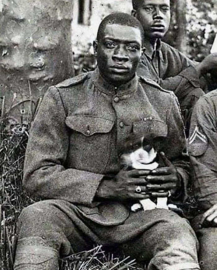 Un miembro de los Harlem Hellfighters (369.º Regimiento de Infantería) posa para la cámara mientras sostiene un cachorro que salvó durante la Primera Guerra Mundial, 1918.