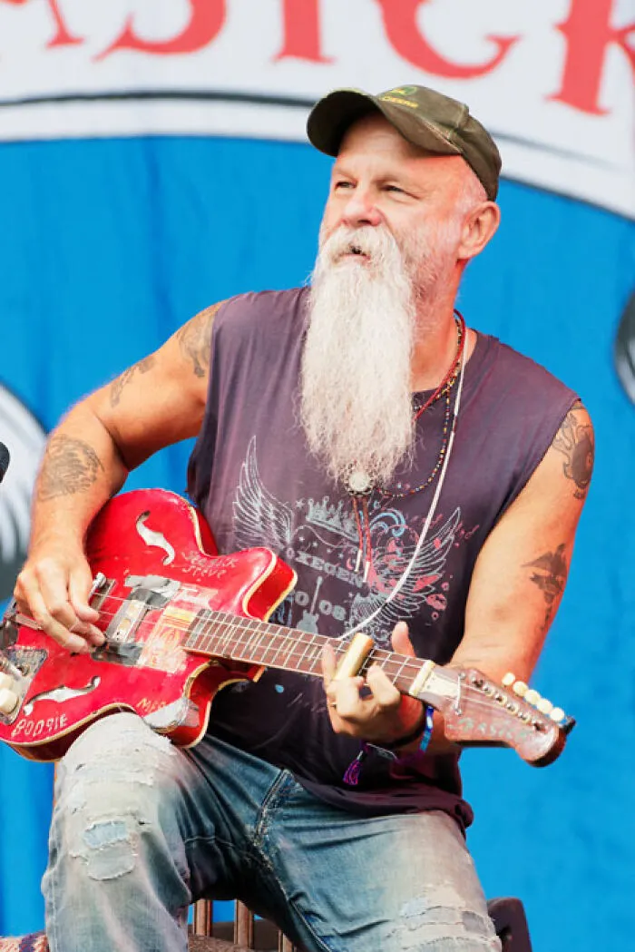 Older man with long white beard playing red guitar, embodying late bloomers who became millionaires after being counted out.