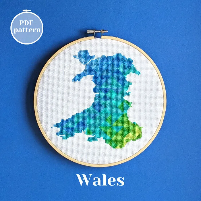 Cross-stitched map of Wales with geometric blue and green patterns in an embroidery hoop on a blue background.