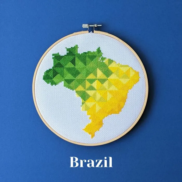Cross-stitched map of Brazil in green and yellow thread displayed in an embroidery hoop on a blue background