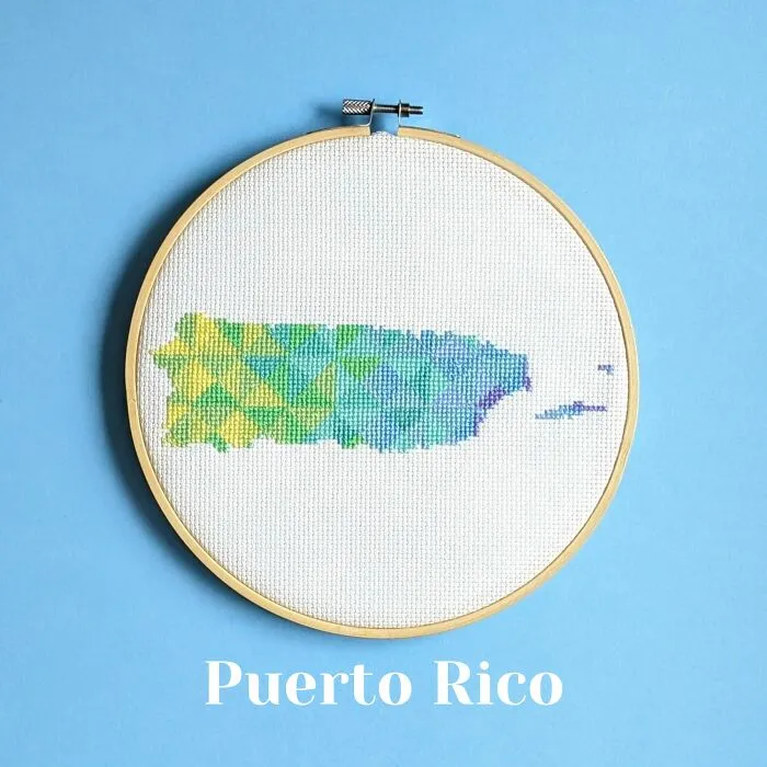 Cross-stitched map of Puerto Rico with colorful geometric patterns in a wooden embroidery hoop on a blue background