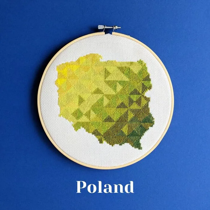 Cross-stitched map of Poland in shades of yellow and green displayed in an embroidery hoop on a blue background.