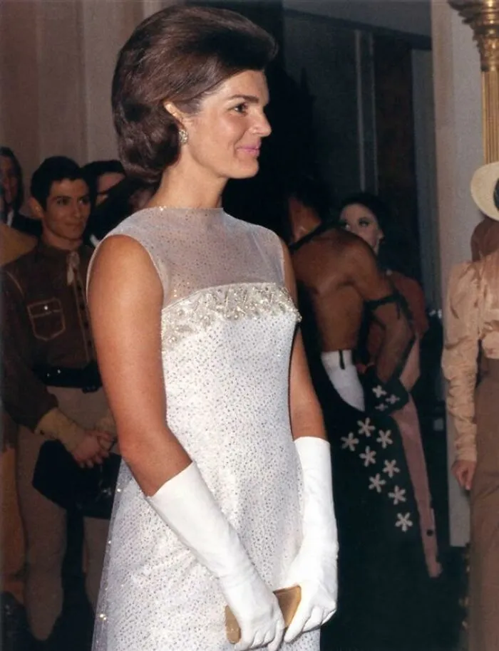 Elegant woman wearing a white gown and gloves at a formal event, showcasing famous names from history known for good looks.