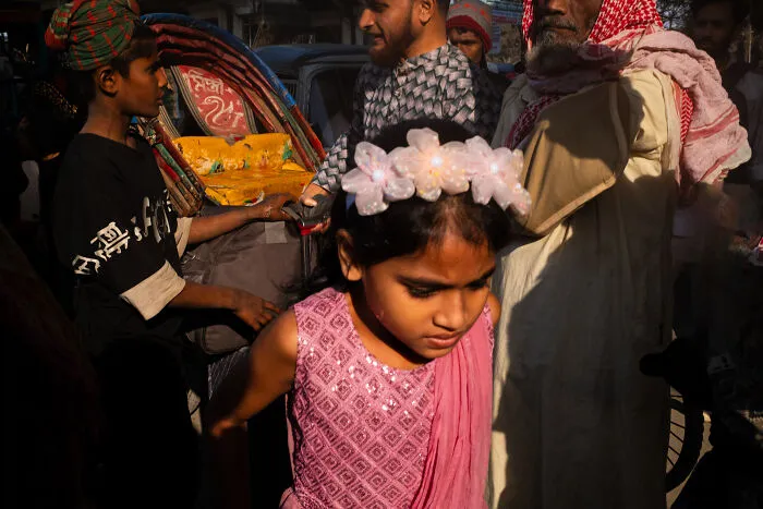 Young girl in a pink dress surrounded by street people, captured candidly by photographer traveling the world.