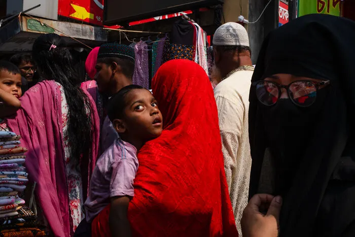Candid street moment showing a woman in red carrying a child among a crowd, capturing emotion and everyday life.