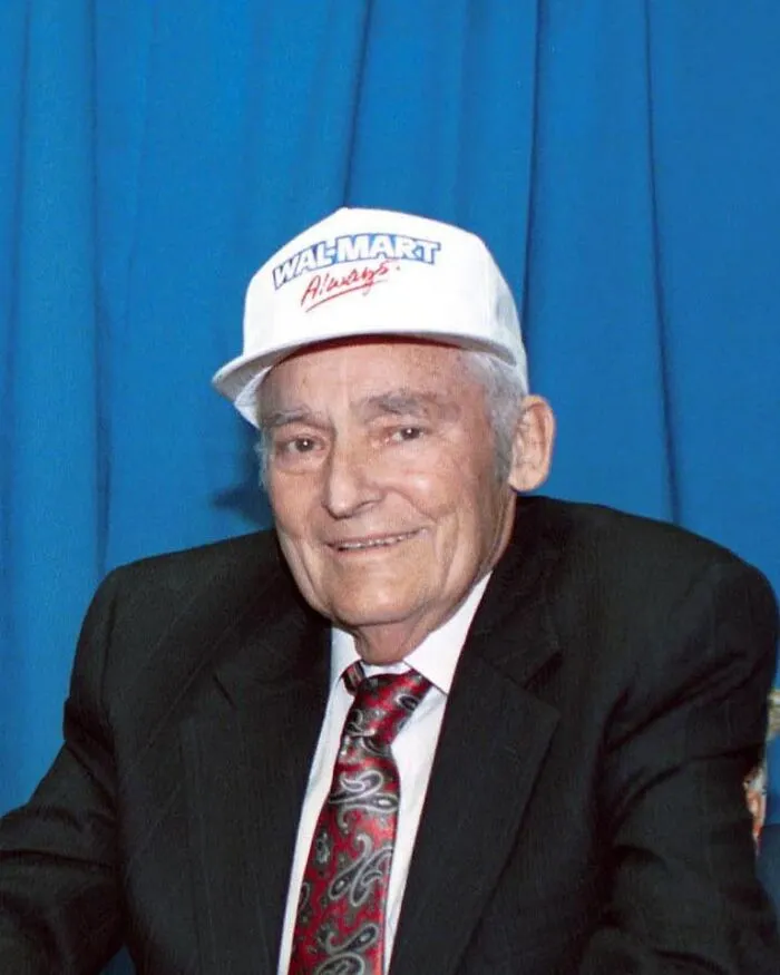 Elderly man in a suit and Walmart hat smiling, representing late bloomers who became millionaires after being counted out.