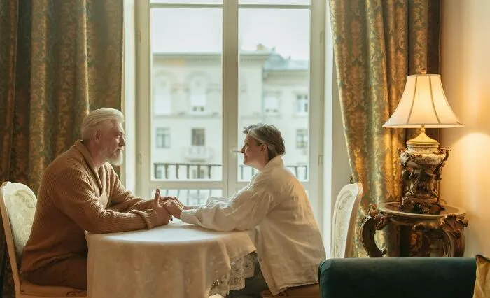 Elderly couple holding hands across table in cozy room, reflecting on moments for then vs now poll discussion.