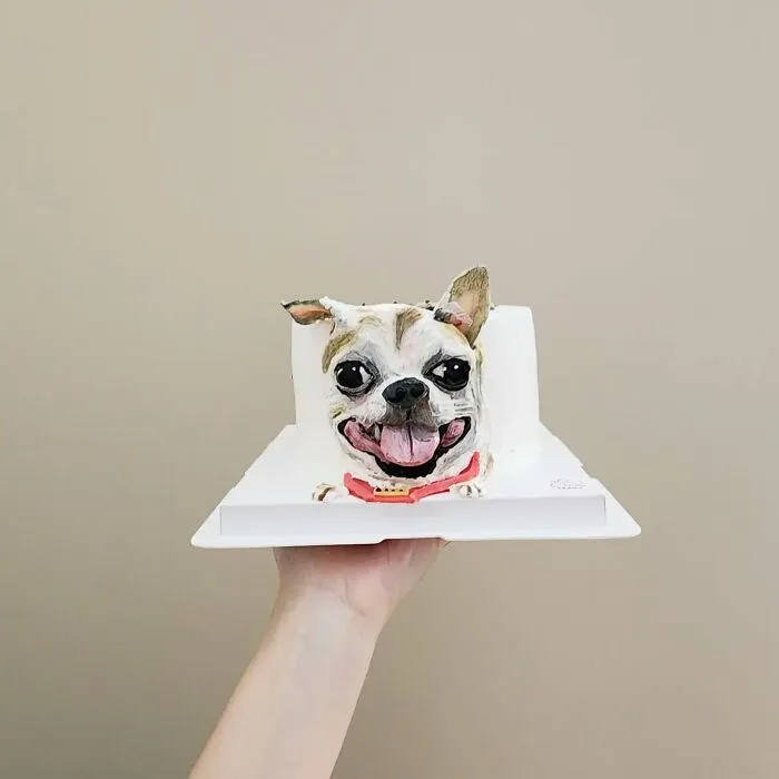 Hand holding an adorable pet-themed cake shaped like a smiling dog, showcasing unique personality in artistic cake design.