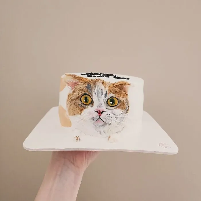 Hand holding a pet-themed cake featuring an adorable, realistic cat face capturing its unique personality.