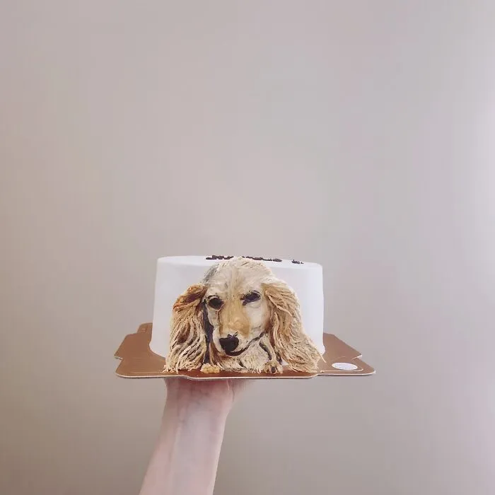 Hand holding a pet-themed cake with a detailed dog portrait, showcasing an artist's adorable pet-themed cake design.