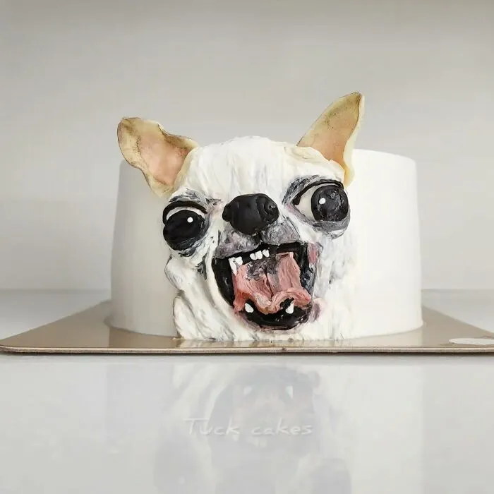 Pet-themed cake shaped like a white dog with exaggerated eyes and tongue, capturing the pet's unique personality in edible art.