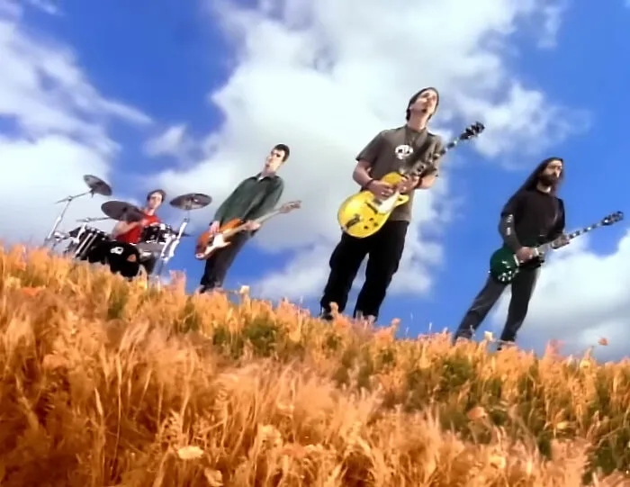Band playing guitars and drums in a wheat field under a blue sky, capturing best I was there when it was written moments.