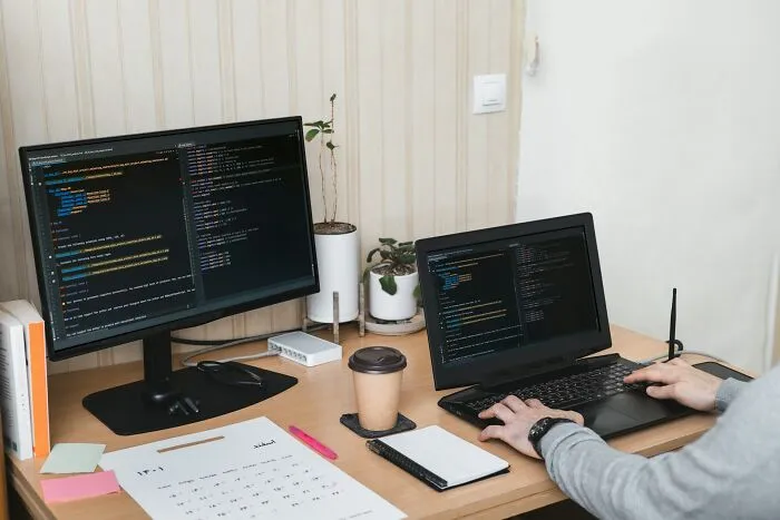Person coding on a laptop and desktop computer, capturing best I was there when it was written moments in a workspace.