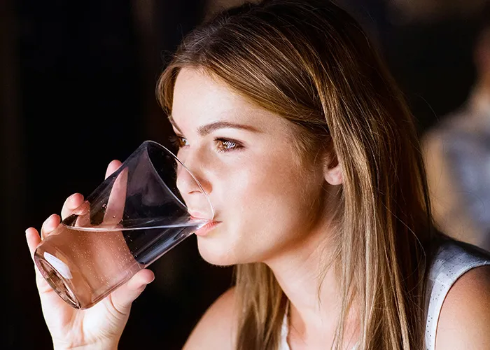 Young woman drinking a glass of water, demonstrating healthy habits that may improve your quality of life.