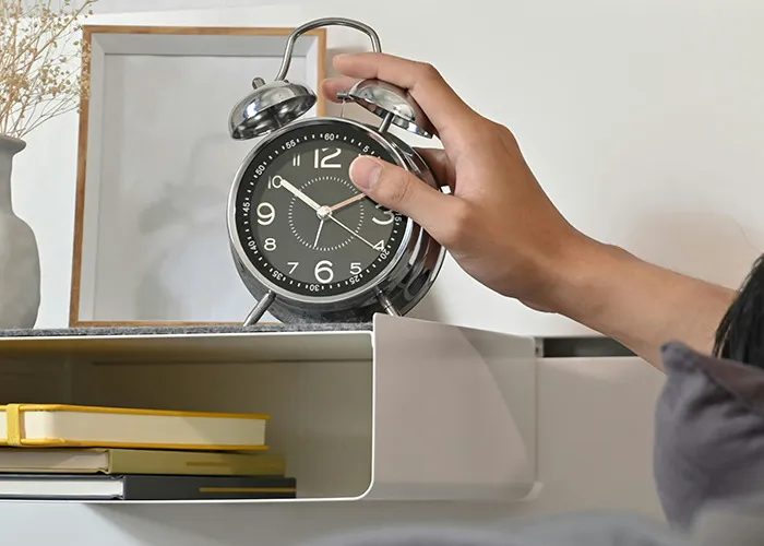 Hand reaching to turn off a vintage alarm clock on a nightstand, symbolizing habits to improve quality of life.