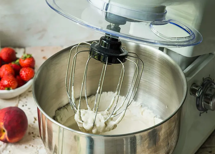 Stand mixer whipping creamy batter in a bowl with fresh strawberries and a peach, illustrating habits to improve quality of life.