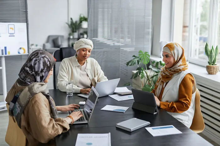Three professional women using laptops in a modern office, discussing ways to call out corporate pals’ lies effectively.