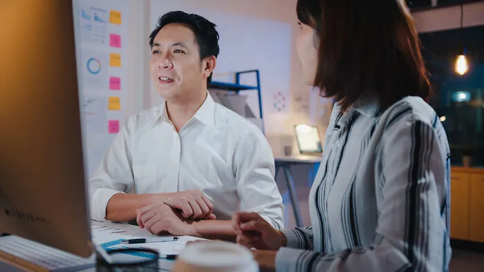 Two colleagues discussing at a desk in a modern office, illustrating ways to call out corporate pals’ lies.