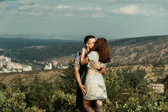 Couple embracing and kissing outdoors with mountains in the background, representing secrets people keep from their lovers.