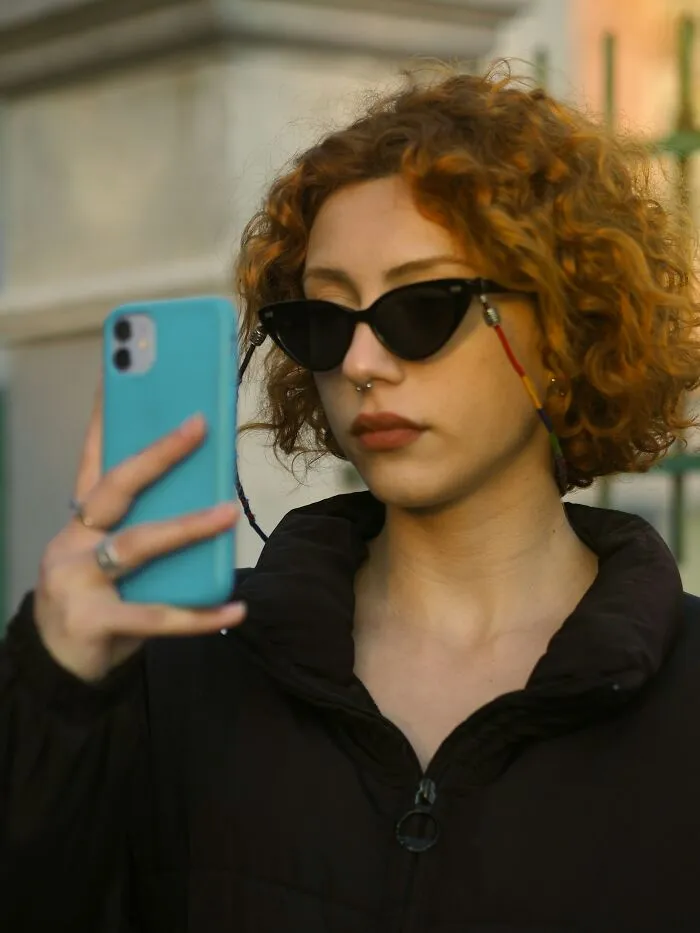Young woman wearing sunglasses using smartphone, reflecting on unique childhood joys lost with smartphones.