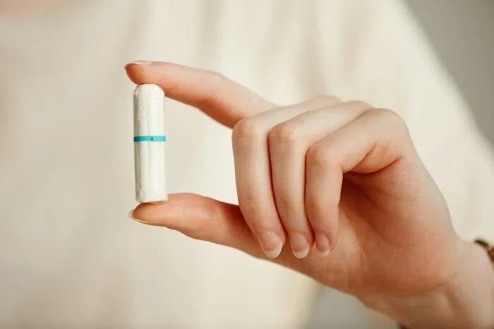 Hand holding a sanitary tampon with a blue stripe, representing postpartum OCD awareness in women's health.
