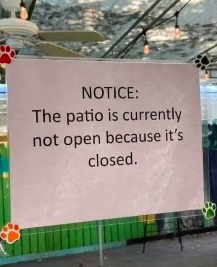 Funny sign on a patio stating it is not open because it is closed, adding chaos with hilarious wording.