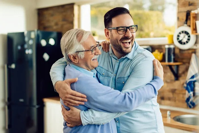 Two men happily hugging in a cozy kitchen, representing people from history who inspire connection and admiration.