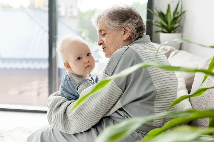 Elderly woman holding baby indoors, representing connection with historical figures people would love to call.