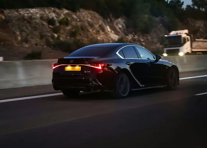 Black Lexus sedan driving on a highway at dusk with blurred background, illustrating historic figures in a modern setting.
