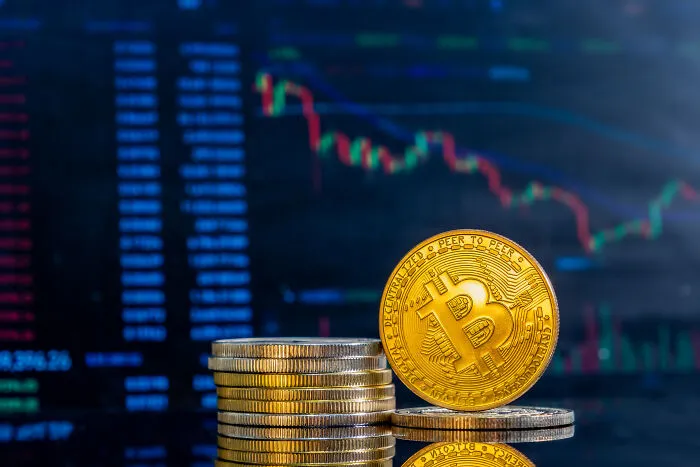 Stack of golden bitcoins in front of a fluctuating digital chart representing historical people of interest.