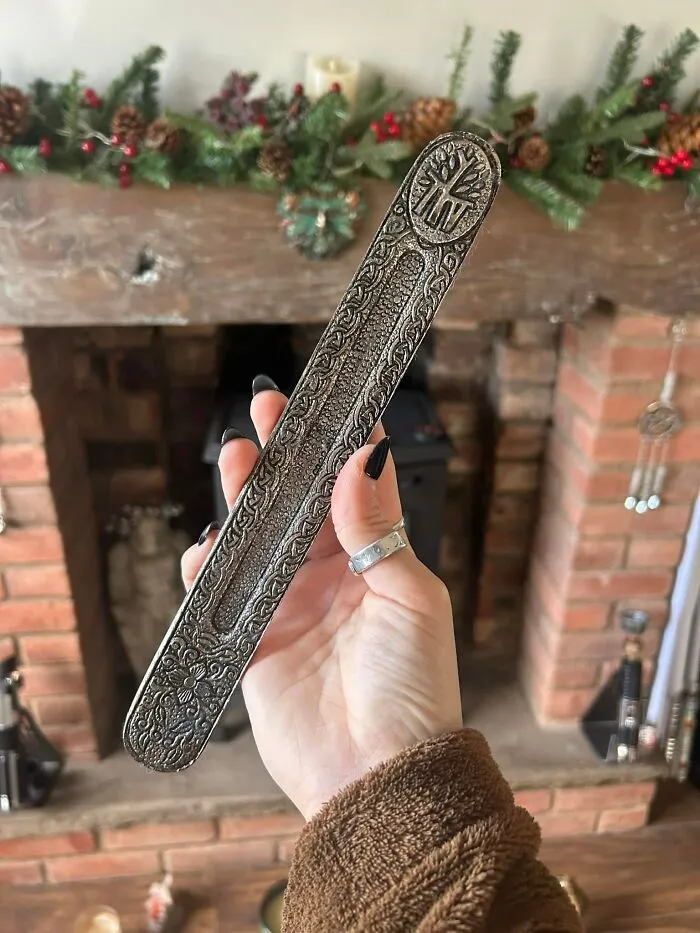 Hand holding an ornate metal object found in walls and other hidden places in people’s homes near a brick fireplace.