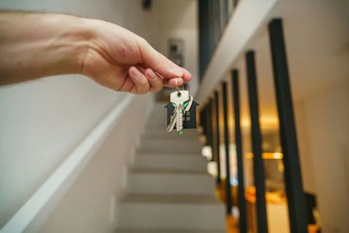 Hand holding house-shaped keychain with keys inside modern home, representing challenges of being big in Japan.