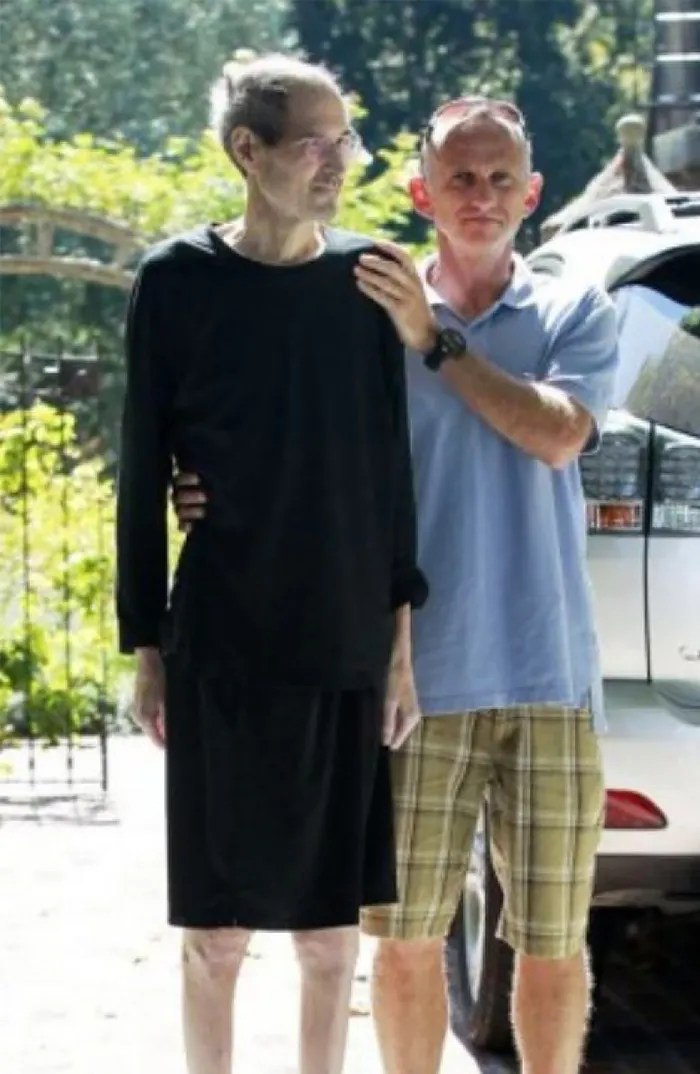 Two men outdoors by a car, one supporting the other, in a candid moment from last known photos of famous people