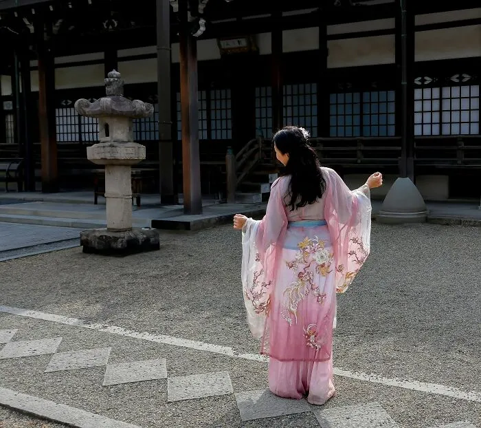 Woman in a traditional pink kimono standing in a Japanese temple courtyard, symbolizing being big in Japan culture.