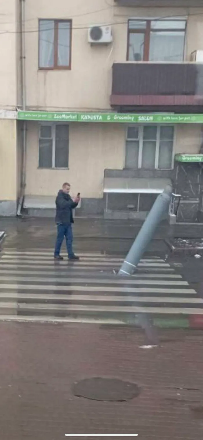 Hombre tomando foto a poste inclinado en paso peatonal, ilustrando razones por las que mujeres viven más que hombres.