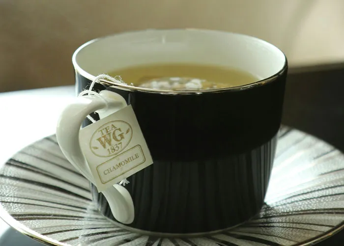 Black cup of chamomile tea with tea bag on a patterned saucer representing healthy foods to skip eating advice