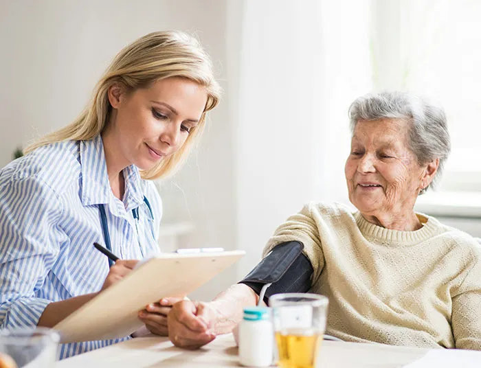 Young female caregiver taking notes while measuring blood pressure of elderly woman at home, illustrating legal claims context.