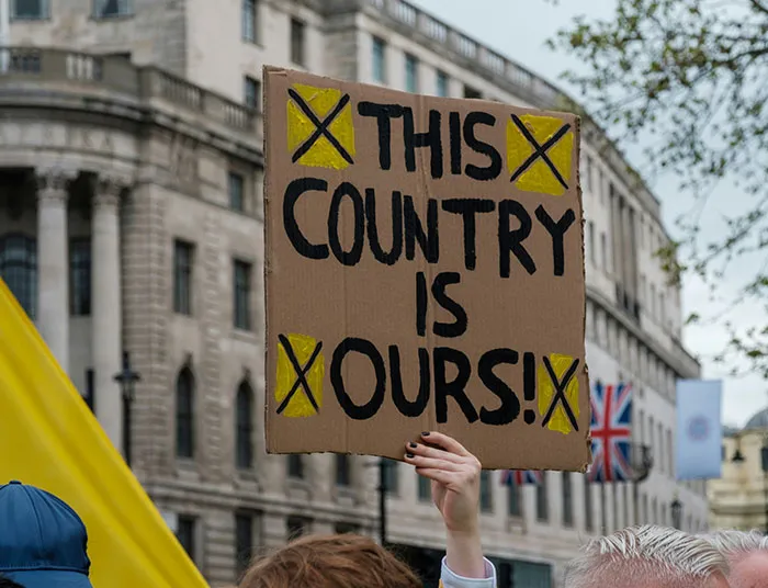 Protester holding a cardboard sign claiming ownership, illustrating absurd legal claims in public demonstration.